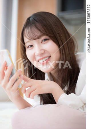 Close-up of a woman relaxing on her smartphone while lying face down. Close-up of a woman relaxing on her smartphone while lying face down. 138667252