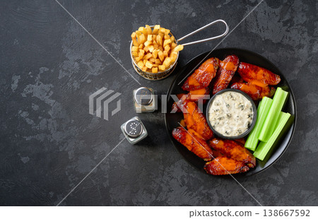 Hot and spicy buffalo chicken wings with fried French fries and dip sauce on a dark table, copy space for text. Top view. Hot and spicy buffalo chicken wings with fried French fries and dip sauce on a dark table, copy space for text. Top view. 138667592