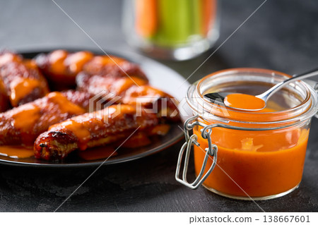 Hot and spicy red Buffalo sauce for chicken wings in a bowl on a dark table. Hot and spicy red Buffalo sauce for chicken wings in a bowl on a dark table. 138667601