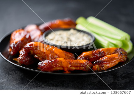 crunchy buffalo chicken wings with celery sticks and blue cheese dipping sauce on a dark table. 138667607
