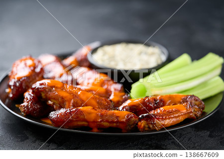 crunchy buffalo chicken wings with celery sticks and blue cheese dipping sauce on a dark table. 138667609