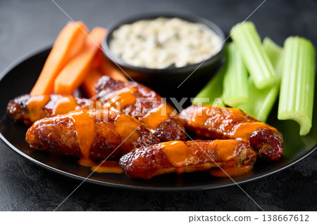 bbq buffalo chicken wings in a plate, with ranch dip, carrot and celery sticks on a dark table. bbq buffalo chicken wings in a plate, with ranch dip, carrot and celery sticks on a dark table. 138667612