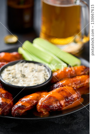 Spicy Buffalo wings with blue cheese sauce and beer with of celery sticks on a dark table. Spicy Buffalo wings with blue cheese sauce and beer with of celery sticks on a dark table. 138667615