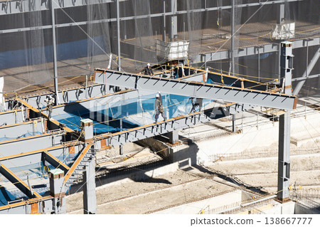 在鋼結構建築工地，四名工人正在引導和安裝由起重機吊起的鋼樑。 138667777