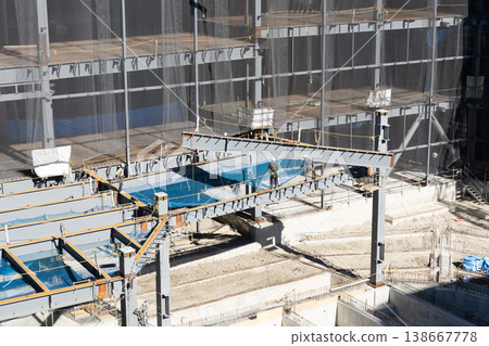 Five workers guide and install a steel beam being lifted by a crane at a steel frame construction site. 138667778