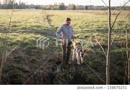Woman walking dog on leash during countryside hike in green spring meadow Woman walking dog on leash during countryside hike in green spring meadow 138670251