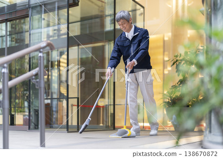Senior building maintenance staff cleaning the building's entrance. Senior building maintenance staff cleaning the building's entrance. 138670872