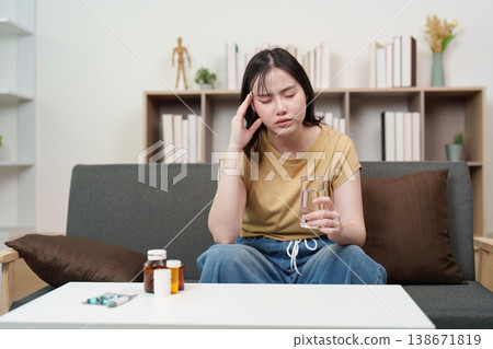 Woman with headache holding a glass of water and medicine Woman with headache holding a glass of water and medicine 138671819