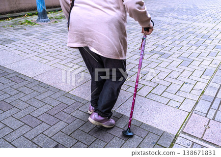 A shuffling gait in the urban landscape of Yokohama, Japan... through gaps... An elderly woman with a cane walks along a long paved sidewalk... What is life? = Yokohama city 138671831