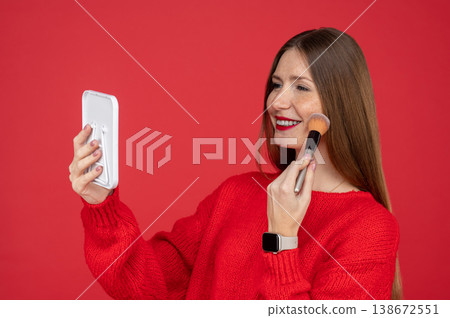 Cheerful young woman with freckles applying makeup with brush while looking in small mirror Cheerful young woman with freckles applying makeup with brush while looking in small mirror 138672551
