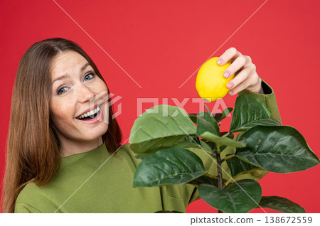 Playful woman placing lemon on houseplant leaves smiling 138672559