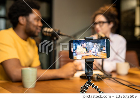 Diverse partners recording video podcast and looking at smartphone Diverse partners recording video podcast and looking at smartphone 138672609