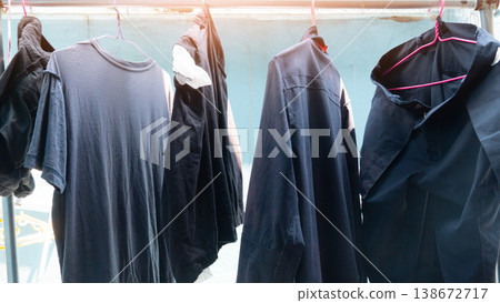 Dark colored shirt and trousers or blue in color. Are hanging on a clothesline outdoors. The background is a light blue house wall illuminated by artificial light. 138672717