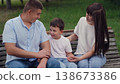 happy family, child parent park, child boy son laughing hugging parent sitting bench park, mother father child having fun hugging outdoors, woman laughing, man laughing, child boy laughing, man woman 138673386