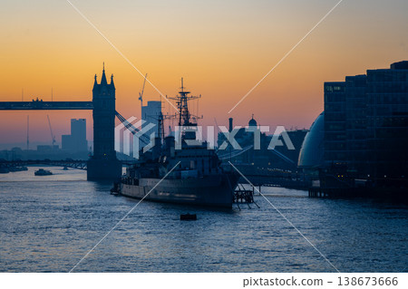Dawn breaks over the river Thames. HMS Belfast sits anchored while Tower Bridge stands silhouetted against the early morning sky in London, United Kingdom. 138673666