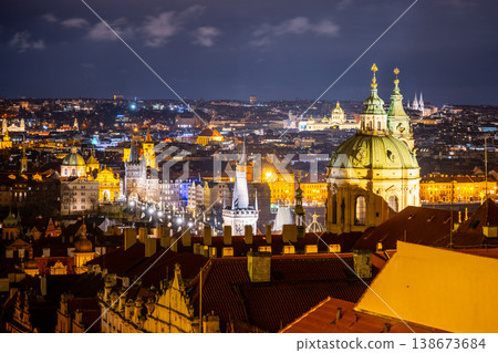 View of St Nicholas Church and Charles Bridge at night in Prague. The city shines with lights. Buildings and rooftops fill the scene. This is a popular area for tourists and locals. View of St Nicholas Church and Charles Bridge at night in Prague. The city shines with lights. Buildings and rooftops fill the scene. This is a popular area for tourists and locals. 138673684