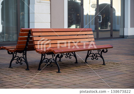 Wooden benches sit on a brick sidewalk in front of a store in a shopping area Wooden benches sit on a brick sidewalk in front of a store in a shopping area 138673822