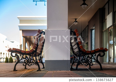 Benches sit side by side under a column in a shopping area during daylight hours Benches sit side by side under a column in a shopping area during daylight hours 138673827