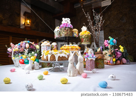Festive Easter dessert table with colorful cakes, eggs, and floral decorations on stone wall Festive Easter dessert table with colorful cakes, eggs, and floral decorations on stone wall 138675483