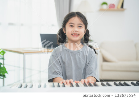 Joyful girl playing piano at home, wearing casual gray t-shirt, smiling in bright living room with modern decor and natural light 138675554