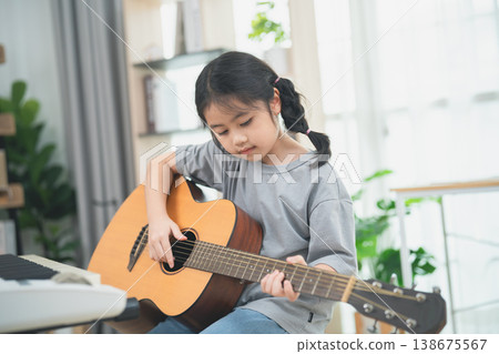 Young girl playing acoustic guitar indoors, enjoying music, developing skills, creative hobby, educating children, artistic expression, passion for music Young girl playing acoustic guitar indoors, enjoying music, developing skills, creative hobby, educating children, artistic expression, passion for music 138675567
