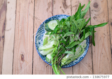 Fresh Thai Basil, Morning Glory and Sliced Cucumber Side Dish on Blue Patterned Plate Wooden Table Fresh Thai Basil, Morning Glory and Sliced Cucumber Side Dish on Blue Patterned Plate Wooden Table 138675977