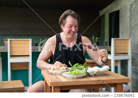 Happy Caucasian Man Eating Grilled Liver Skewer with Thai Isan Food at Outdoor Restaurant Table Happy Caucasian Man Eating Grilled Liver Skewer with Thai Isan Food at Outdoor Restaurant Table 138676091