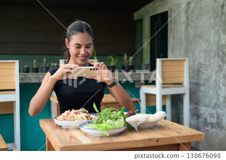 Young Thai Woman Taking Photo of Thai Food with Smartphone for Social Media in Outdoor Restaurant Young Thai Woman Taking Photo of Thai Food with Smartphone for Social Media in Outdoor Restaurant 138676098