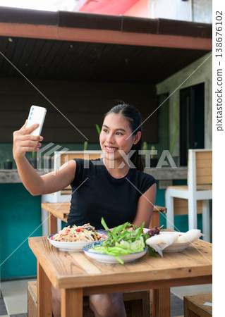 Young Thai Woman Taking Selfie with Smartphone at Restaurant with Traditional Isan Food Vertical 138676102