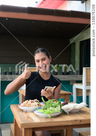 Happy Thai Woman Giving Thumbs Up with Smartphone and Traditional Isan Food Vertical Copy Space Happy Thai Woman Giving Thumbs Up with Smartphone and Traditional Isan Food Vertical Copy Space 138676108