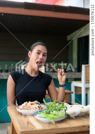 Young Thai Woman Eating Grilled Meat Skewer with Traditional Isan Food at Outdoor Restaurant Vertical Young Thai Woman Eating Grilled Meat Skewer with Traditional Isan Food at Outdoor Restaurant Vertical 138676112