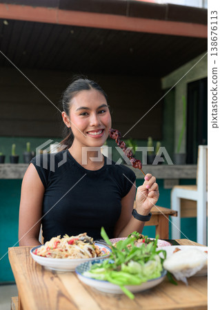 Young Thai Woman Holding Grilled Liver Skewer with Traditional Isan Thai Food at Restaurant Vertical Young Thai Woman Holding Grilled Liver Skewer with Traditional Isan Thai Food at Restaurant Vertical 138676113