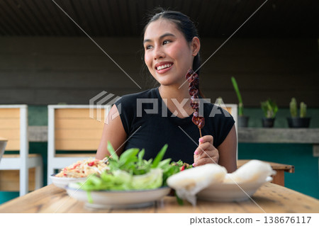 Smiling Thai Woman Holding Grilled Liver Skewer with Traditional Isan Food at Outdoor Restaurant 138676117
