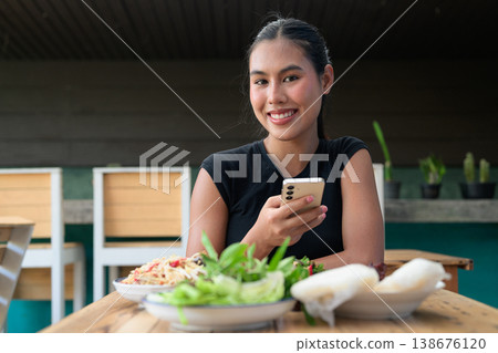 Smiling Young Thai Woman Using Smartphone at Restaurant Table with Traditional Isan Food Copy Space 138676120