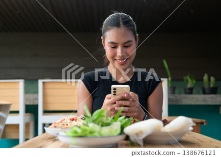 Young Thai Woman Using Smartphone at Restaurant Table with Traditional Isan Food Copy Space 138676121