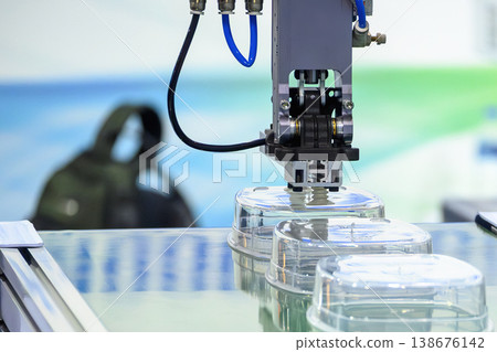 Industrial robotic arm placing plastic food containers onto a conveyor belt from an injection molding machine. 138676142