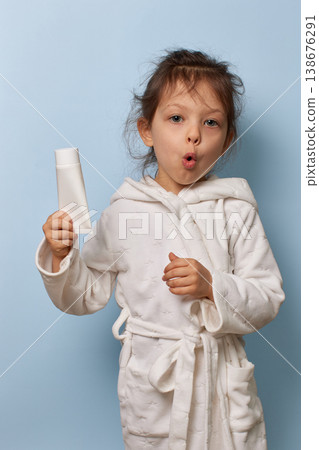 Young child girl in a white bathrobe presenting a clean tube for hygiene against a blue background 138676291