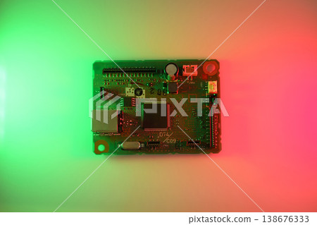Colorfully lit circuit board (PCB) featuring a central microchip, connectors and electronic components on a red-to-green gradient background. Technology, innovation, electronics design. Colorfully lit circuit board (PCB) featuring a central microchip, connectors and electronic components on a red-to-green gradient background. Technology, innovation, electronics design. 138676333