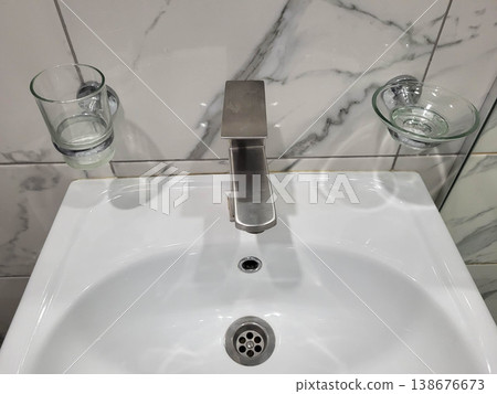 The bathroom has a white handwashing sink with glass accessories The bathroom has a white handwashing sink with glass accessories 138676673