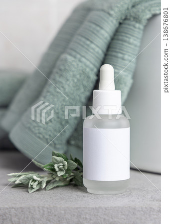 Dropper bottle with blank label mockup near leaves and sage green bath towel. Cosmetic packaging 138676801