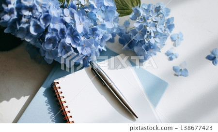 一張白色書桌上放著打開的筆記本和鋼筆，還有繡球花。 138677423