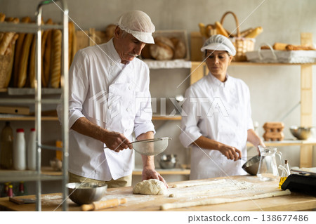 Elderly man and woman sift flour and whipping dough Elderly man and woman sift flour and whipping dough 138677486