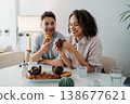 Joyful Pastry Sharing. Two People Delighting In Baked Goods With Cheerful Expressions In Warm Kitchen Setting 138677621