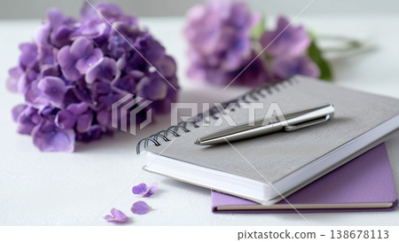 一張白色書桌上放著打開的筆記本和鋼筆，還有繡球花。 138678113