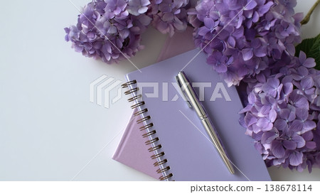 一張白色書桌上放著打開的筆記本和鋼筆，還有繡球花。 138678114