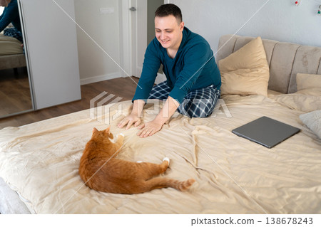 A young caucasian 35 old caucasian man play with their ginger cat on a bed 138678243