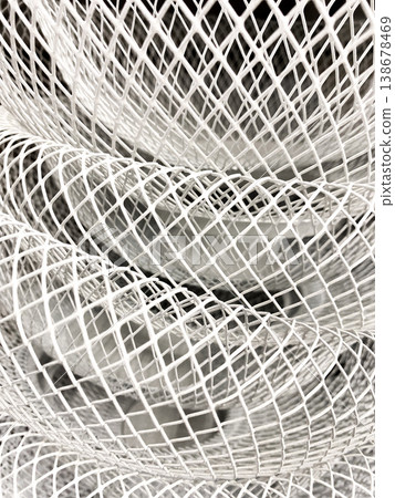 Layered arrangement of white wire mesh formed into curves and spirals. Light highlights gaps and lines in material, interesting patterns. Thin wires twisted together to form large, open shape 138678469