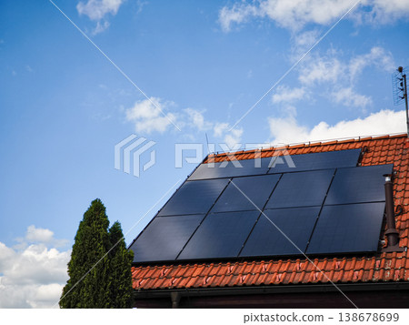 Solar panels installed on a residential roof under a bright blue sky with fluffy clouds showcasing renewable energy technology and sustainability concept 138678699