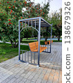 Modern wooden park swing bench on a metal frame surrounded by green trees in a city garden. 138679326