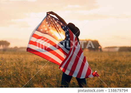Woman farmer in the agricultural field with american flag on sunset. 138679794